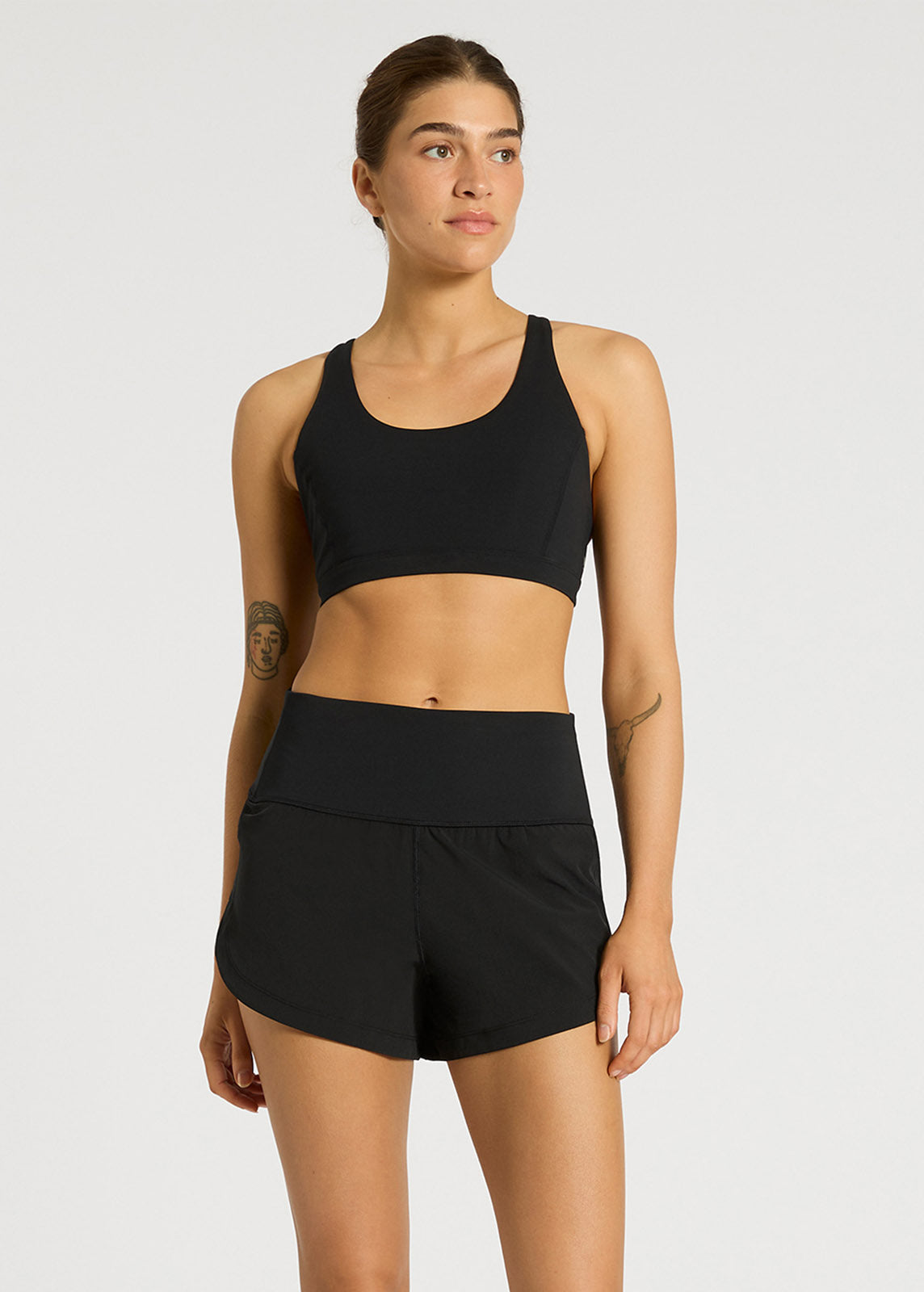 Model wearing black high-rise running shorts and matching sports bra in studio
