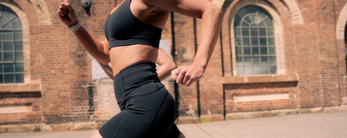 Side profile of a runner in Nimble In Pace activewear running past a brick building.