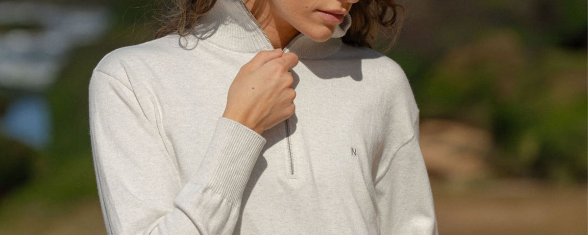 Close-up of woman zipping a light-coloured half-zip sweater outdoors.