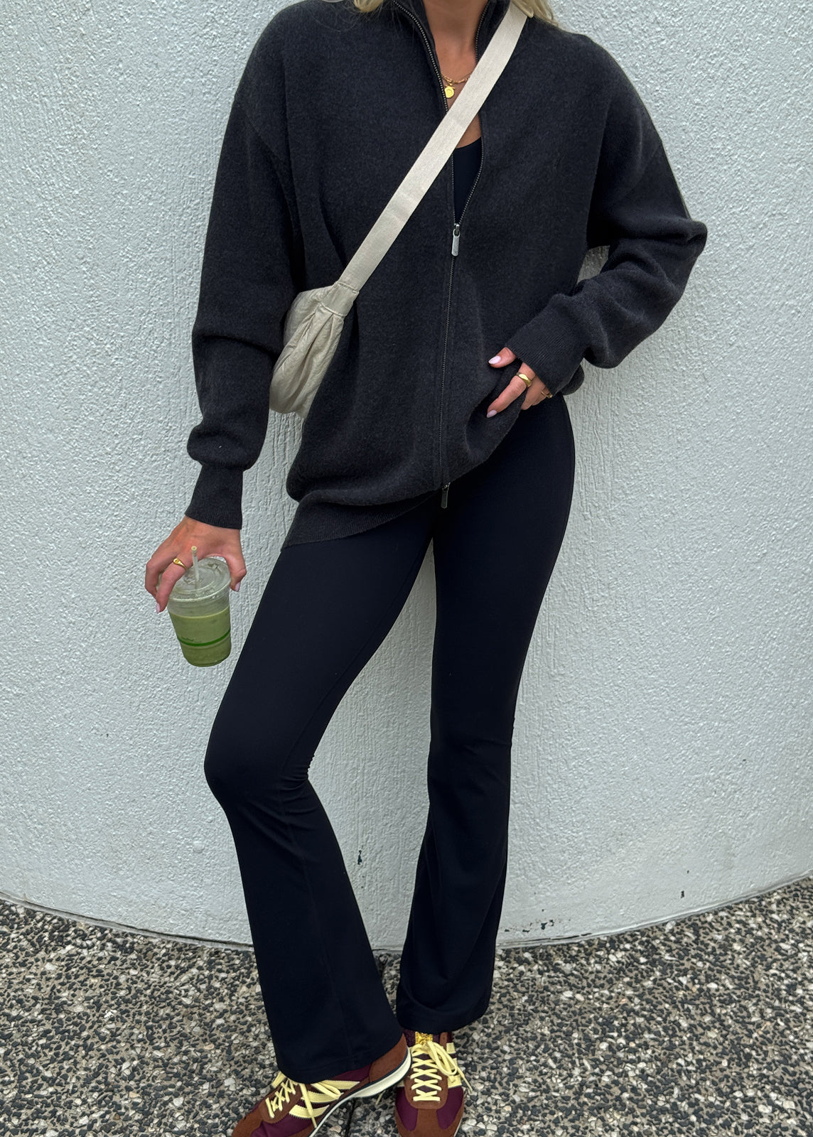 Model wearing black flared leggings and zip sweater holding a smoothie